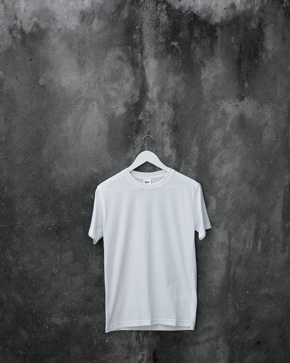 White crew-neck t-shirt hanging on a hanger against textured concrete