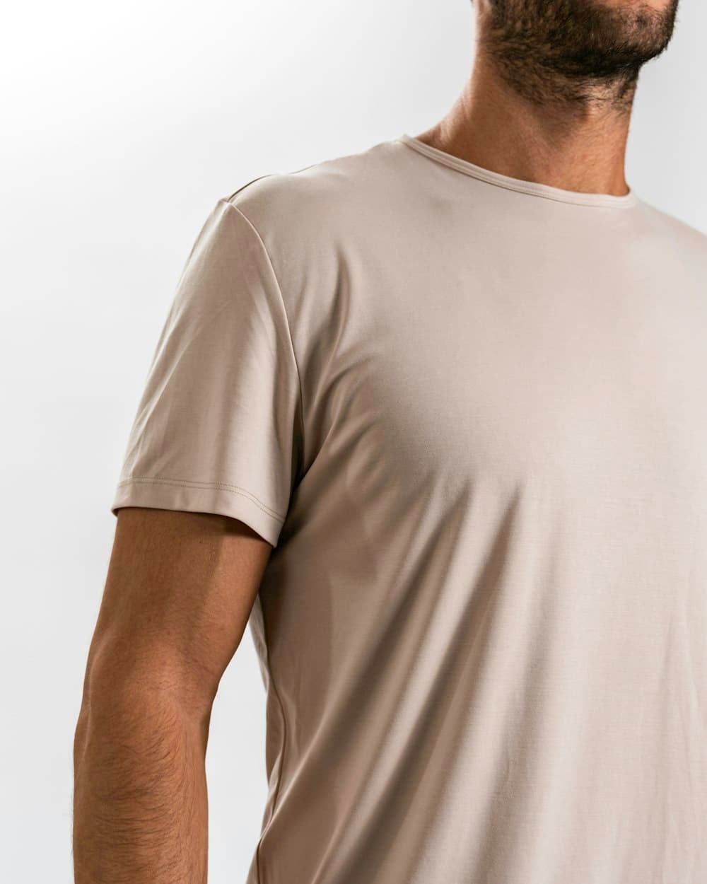 Close-up of a man wearing a sand-colored crew-neck undershirt in soft studio light