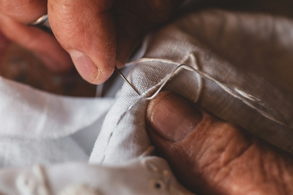 Close-up of hands stitching light fabric with needle and thread